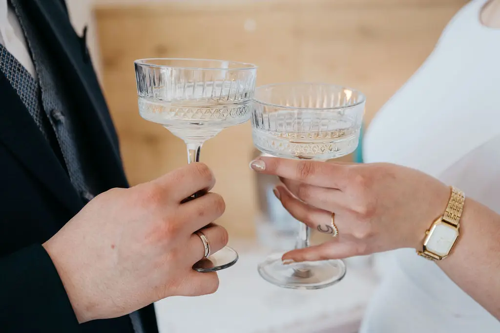Ein frisch vermähltes Paar stößt mit stilvollen Champagnergläsern an – ein besonderer Moment bei einer Hochzeit oder einem Elopement am Tegernsee.