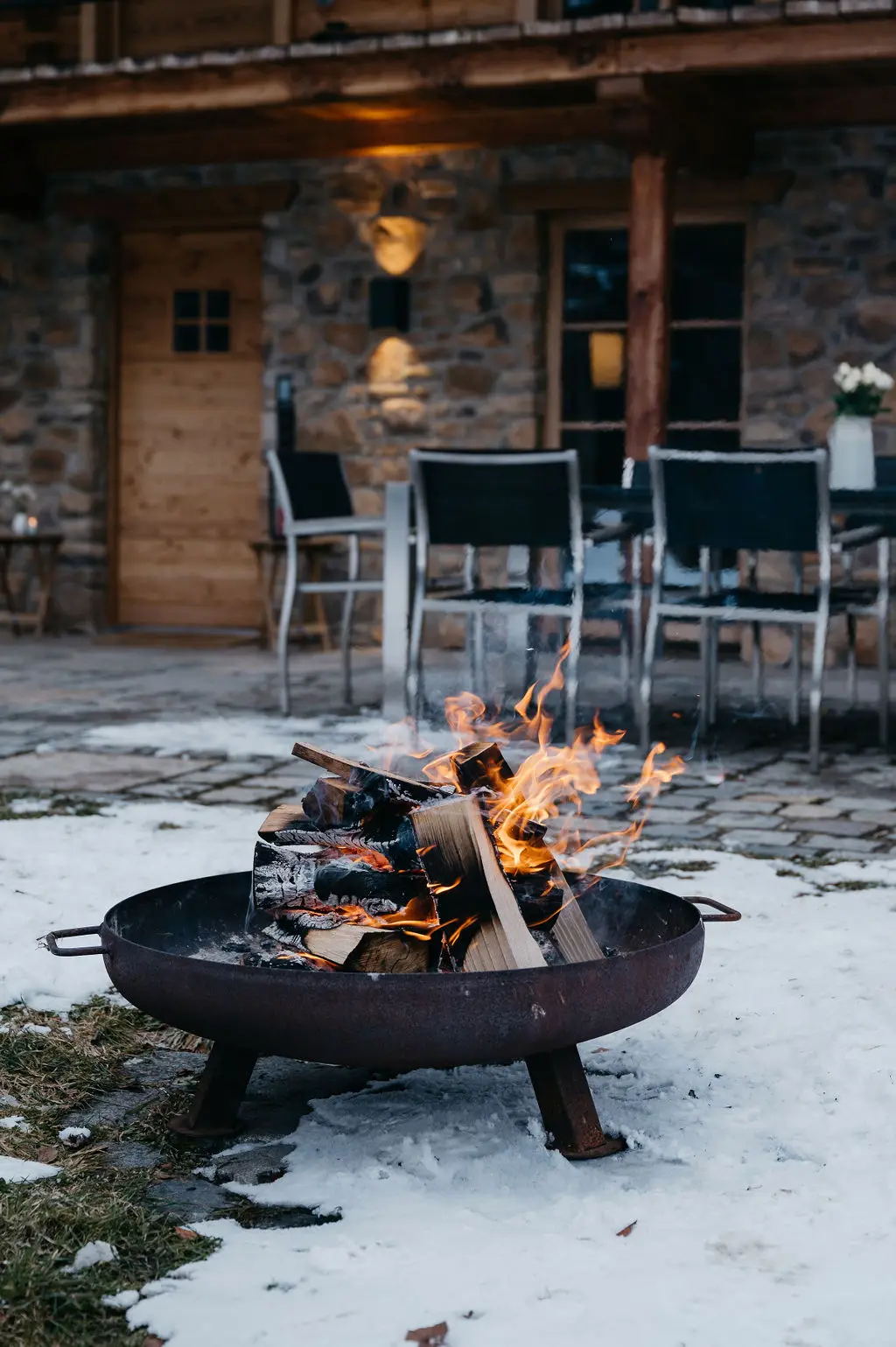 in knisterndes Lagerfeuer vor einer rustikalen Berghütte mit Schneebedeckung – ein stimmungsvoller Moment für ein Winter-Elopement.