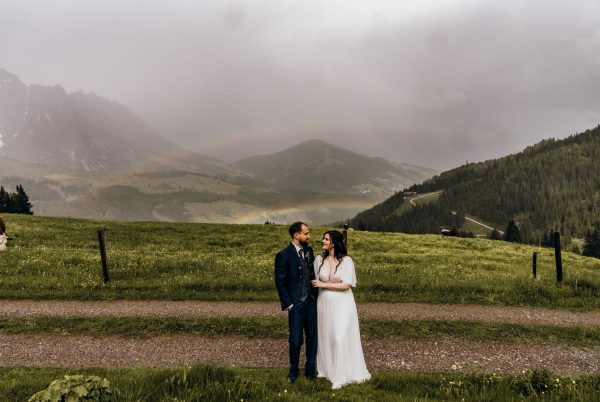 Ein Brautpaar in den Bergen mit einem Regenbogen im Hintergrund