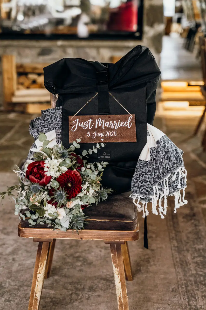 „Just Married“-Schild an einem Rucksack mit Brautstrauß – Details einer Almhochzeit im Juni.