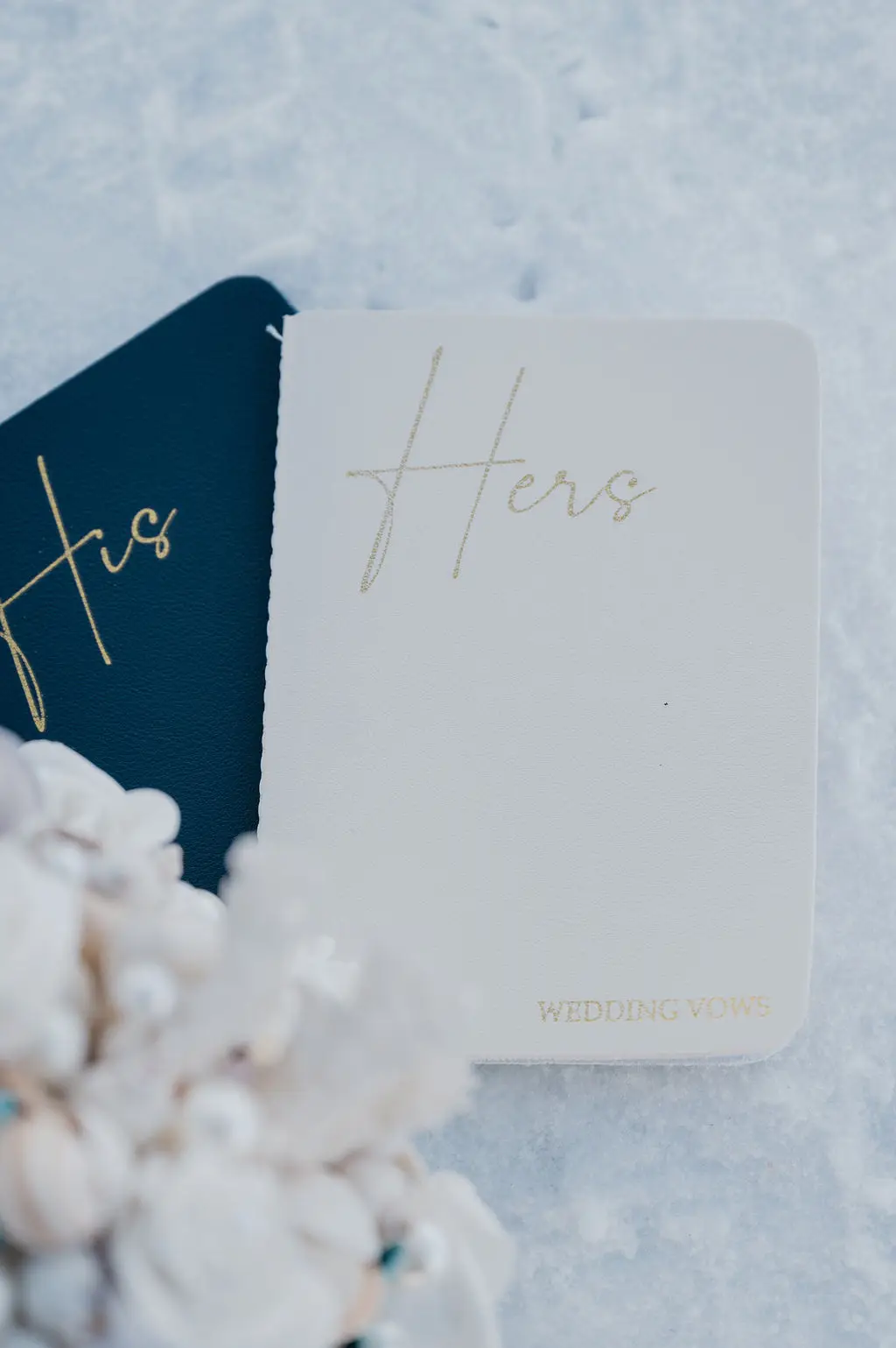 Zwei elegant gestaltete Eheversprechen-Bücher mit “His” und “Hers” Schriftzug auf Schnee – ein intimer Moment bei einer Hochzeit am Tegernsee.